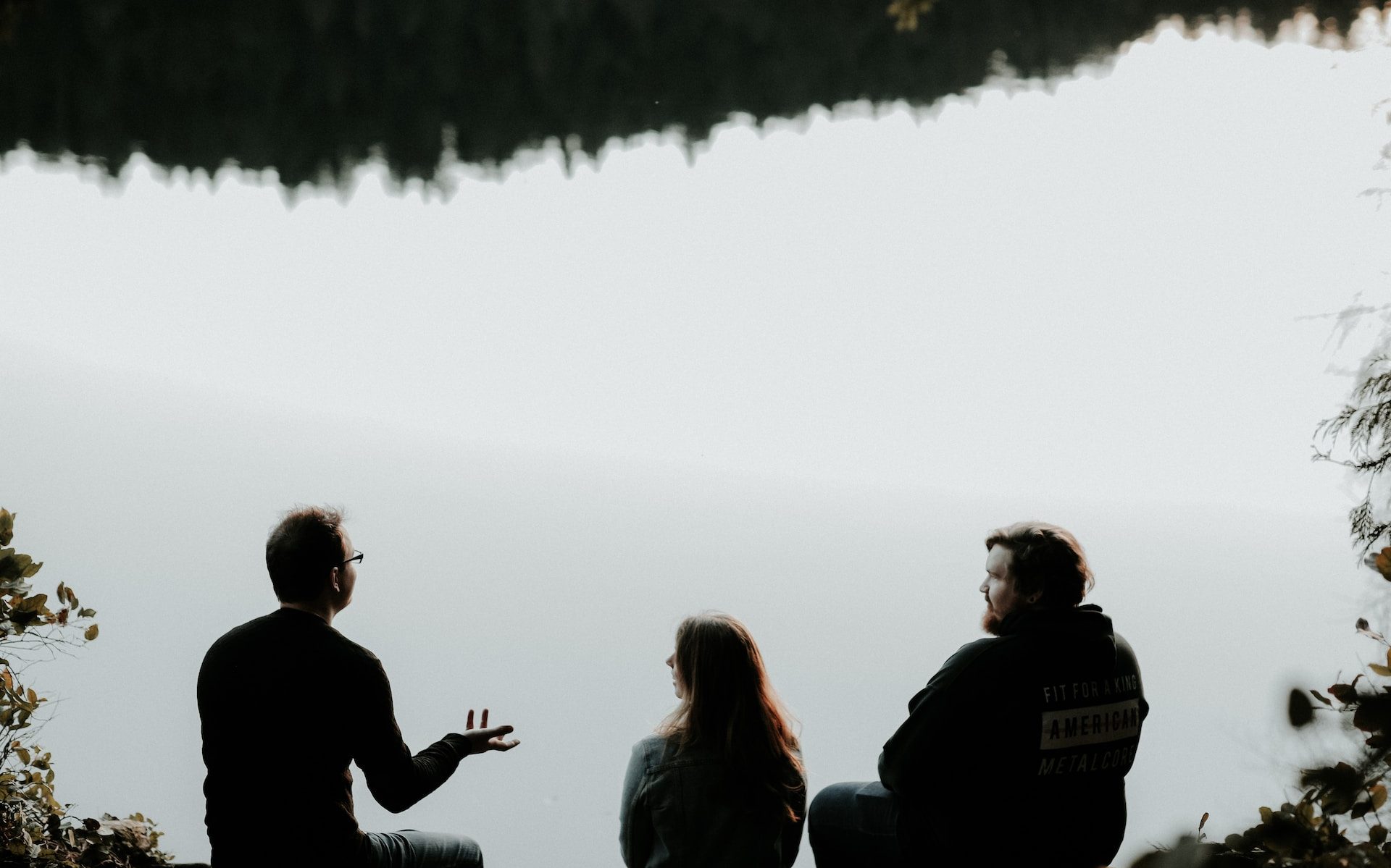 silhouette of three people sitting on cliff under foggy weather